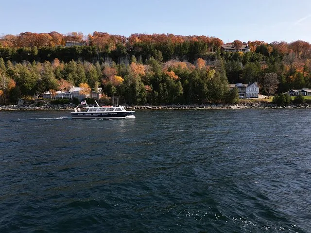 Ein Ausflugsboot, das entlang einer bewaldeten Küste mit Herbstfarben fährt.